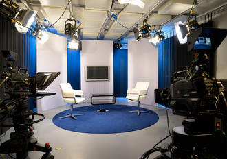 Aufnahme vom Innenbereich des TV-Studios im mbw Haus der Bayerischen Wirtschaft. Setting, Einrichtung in blau, weiß, mit zwei Sesseln, Beistelltisch, Monitor, blauer Teppich, zwei Studiokameras